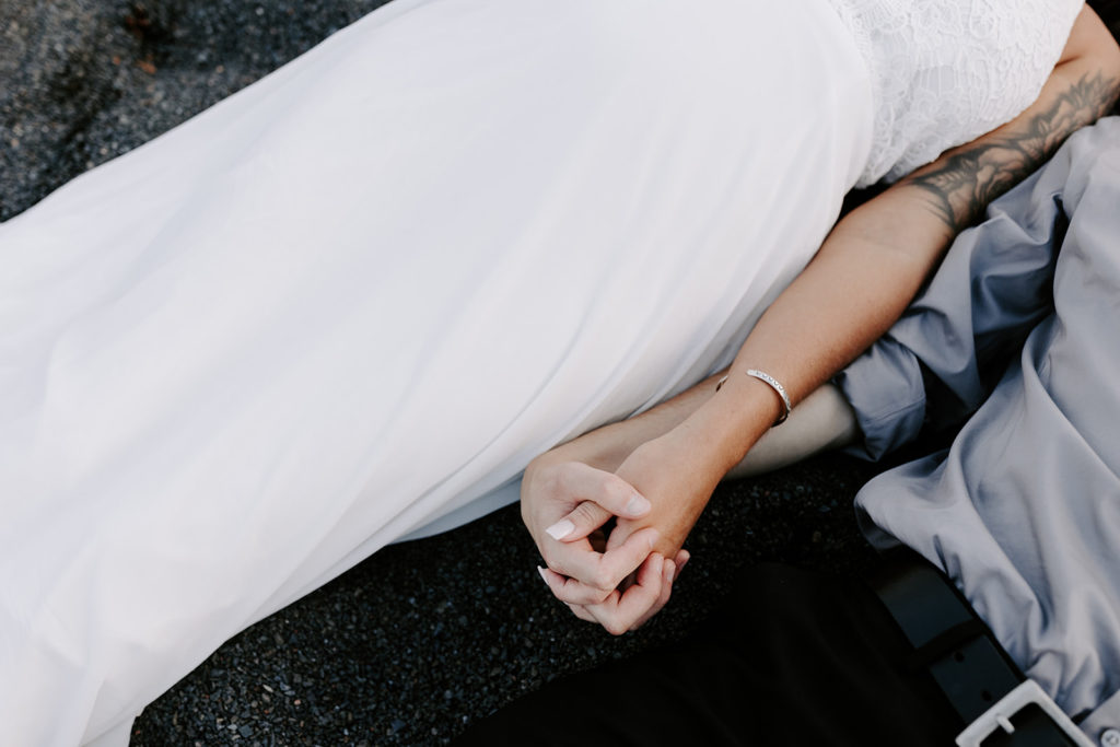 Bride and Groom laying in the sand, holding hands, on Black Beach in Minnesota.