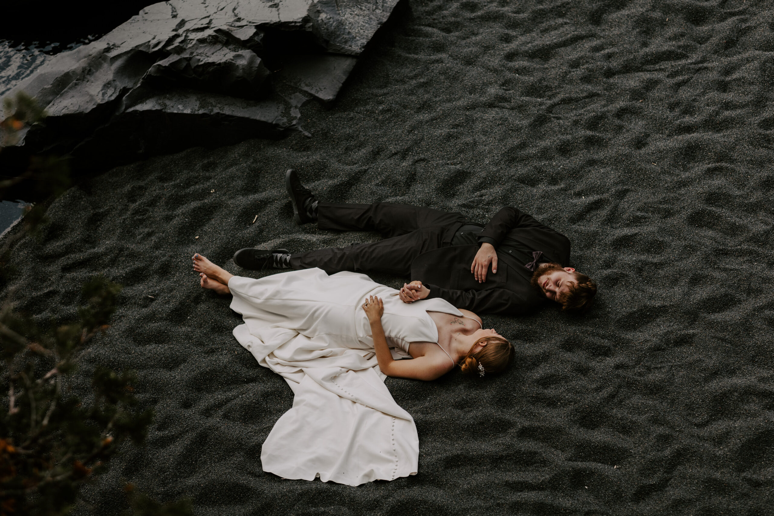 bride and groom laying down together and holding hands on the black beach in minnesota