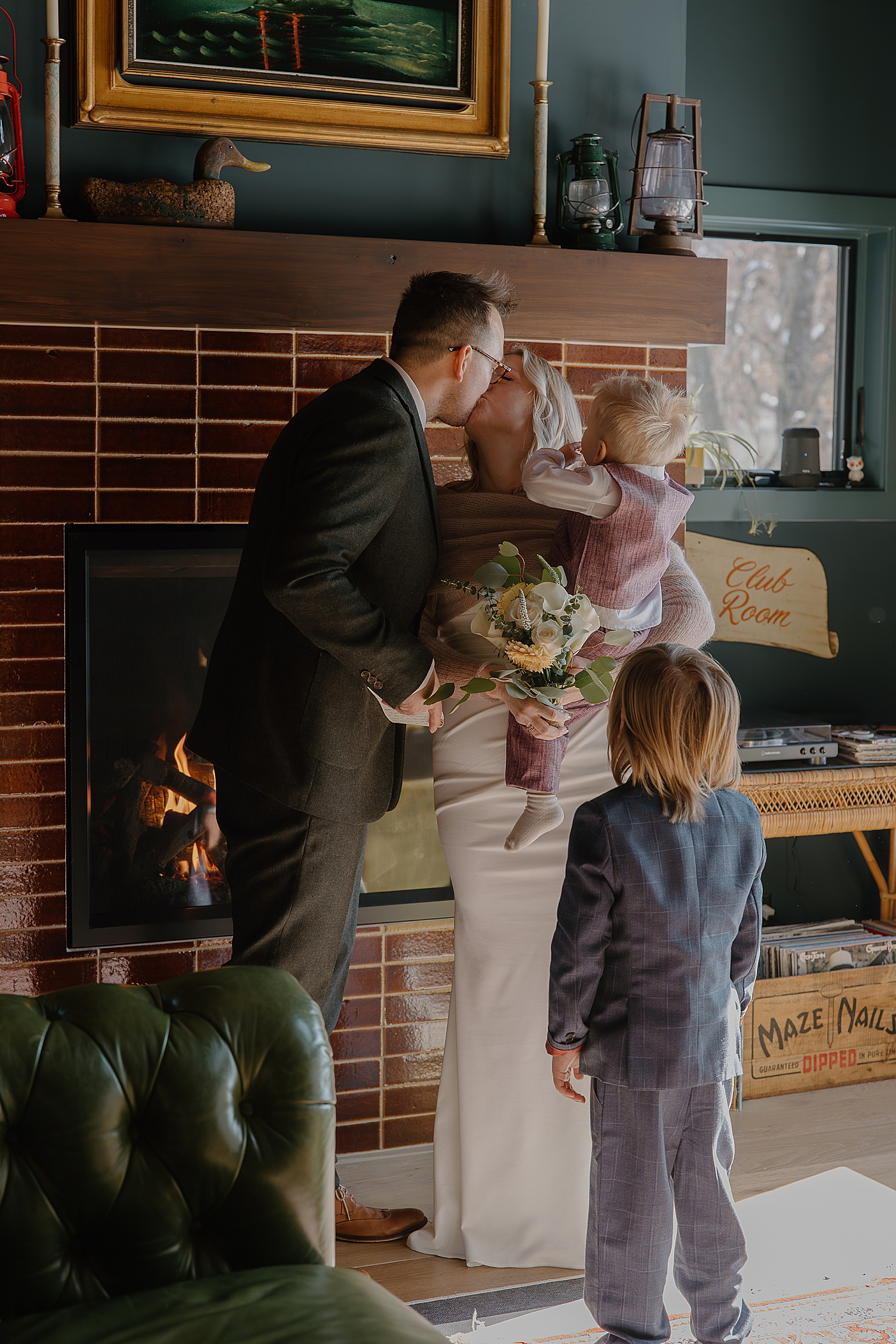 couple share a kiss in front of cozy fire with their kids around by Wisconsin wedding photographer
