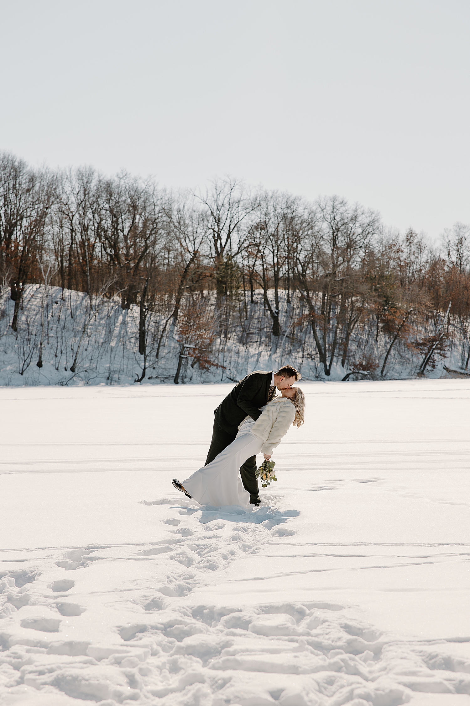 man dips wife for kiss in snowy field for airbnb elopement