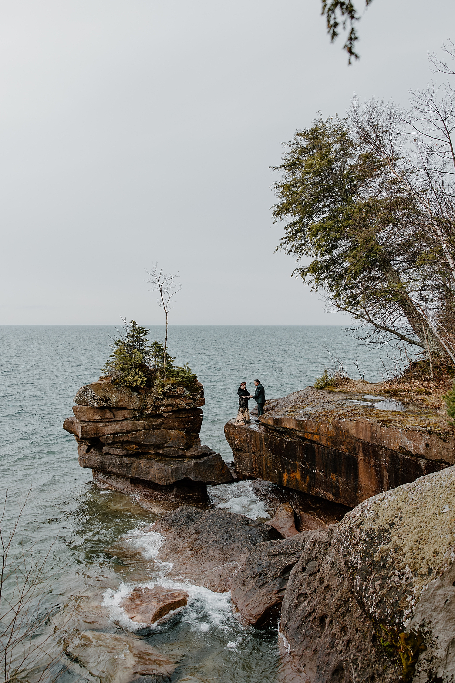 man and wife stand on cliffside overlooking water for Beltane Elopement