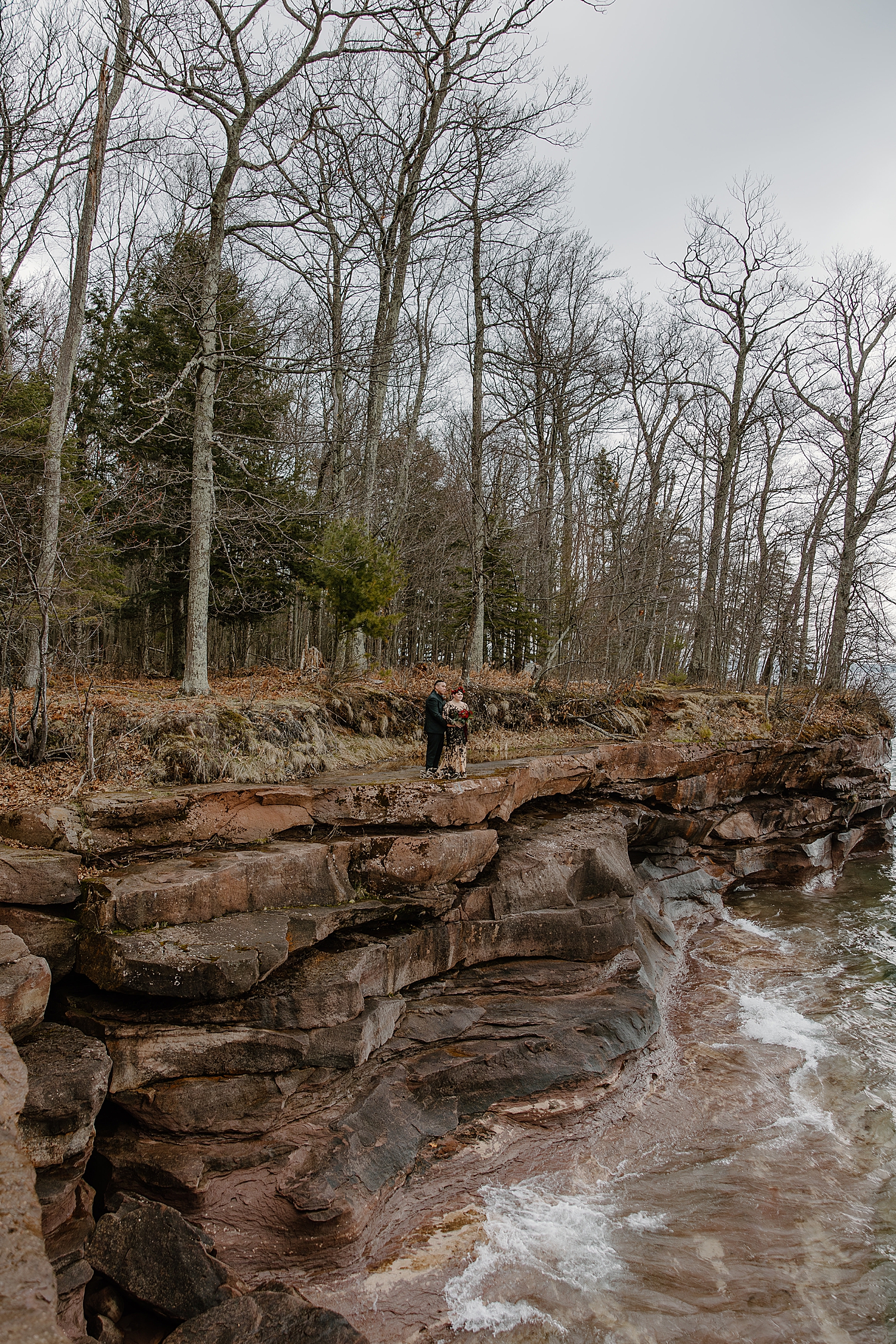 newlwyeds stand on cliffside looking over the water by Wisconsin wedding photographer