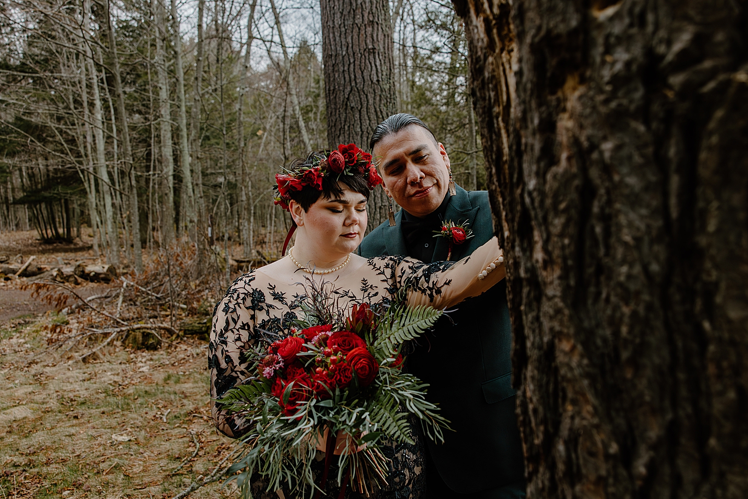 woman with red flower crown places hand on tree with husband by Wisconsin wedding photographer
