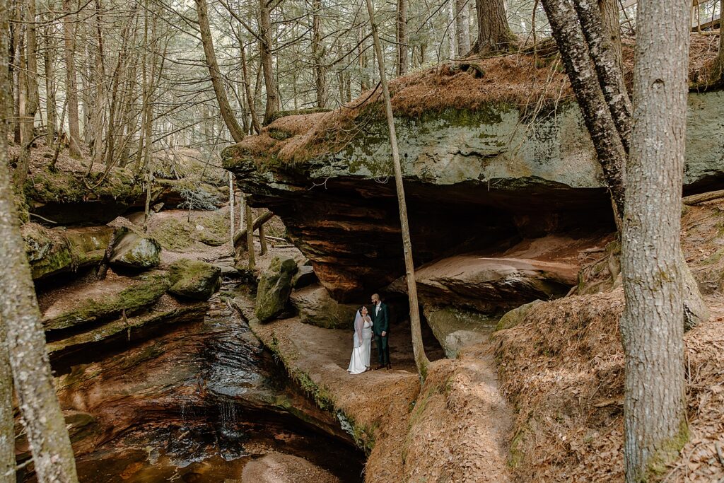 couple hold hands under small forest waterfall by Minnesota elopement photographer