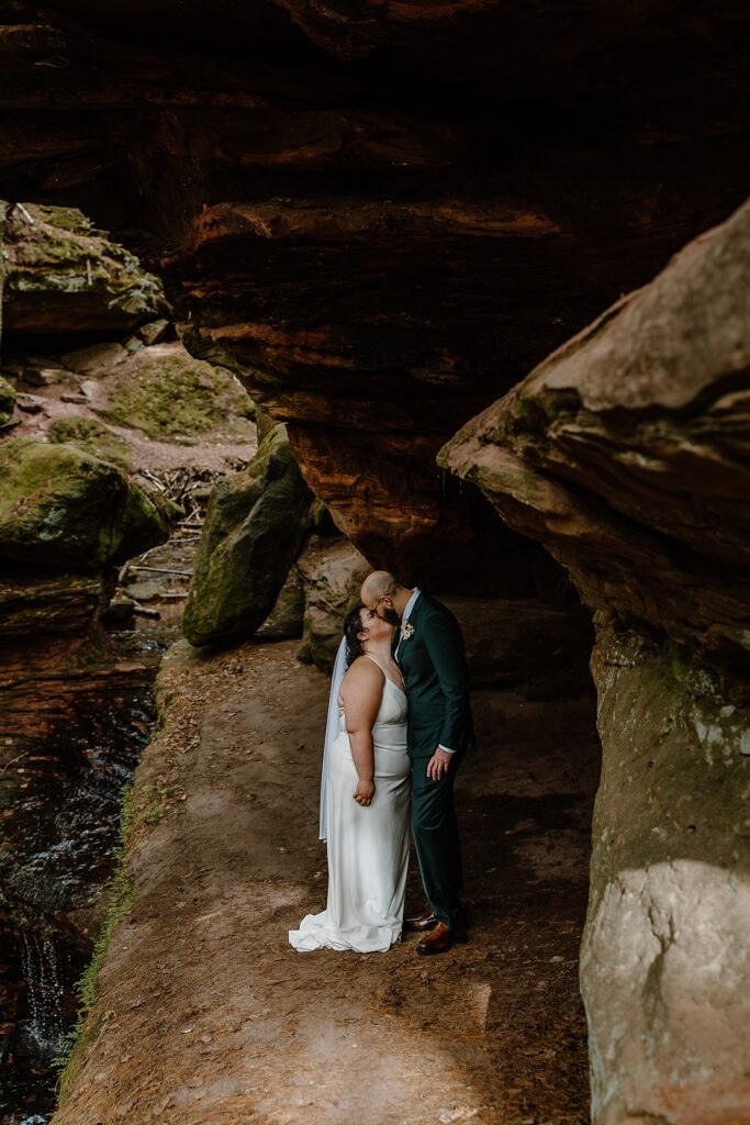 man leans down to kiss bride under rock formation by Samantha Burke Photography