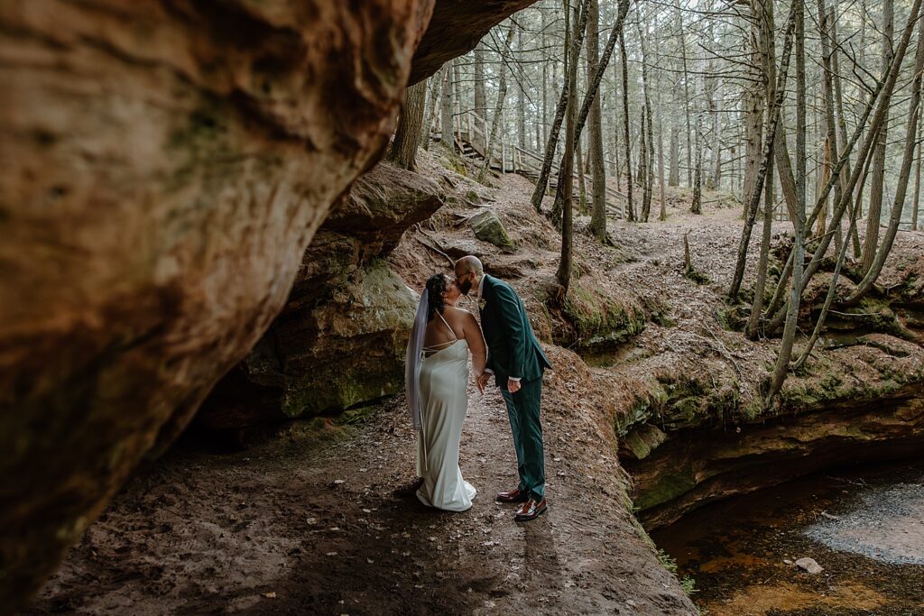 man leans in to kiss his bride under rock for Intimate Ceremony at Houghton Falls