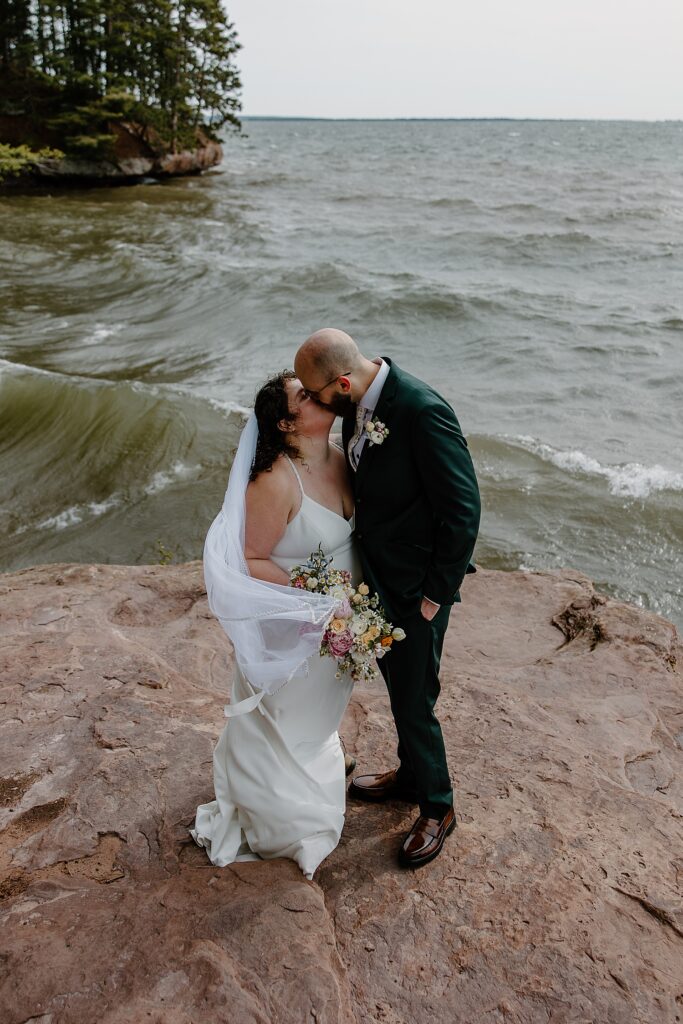 newlyweds kiss on shoreline for Intimate Ceremony at Houghton Falls
