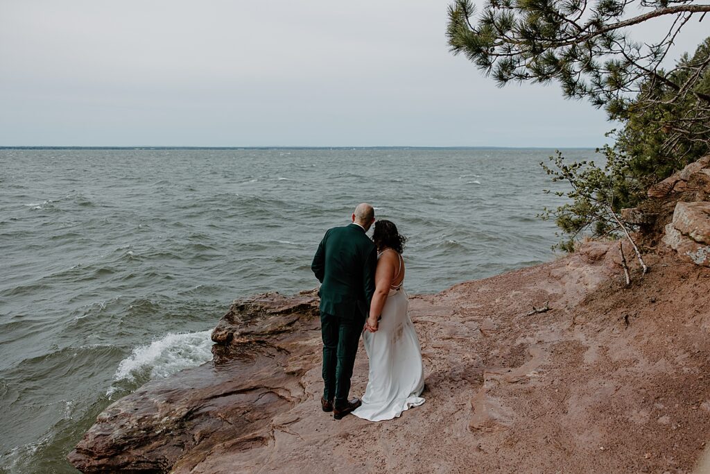 newlyweds hold hands and look over water expanse by Samantha Burke Photography