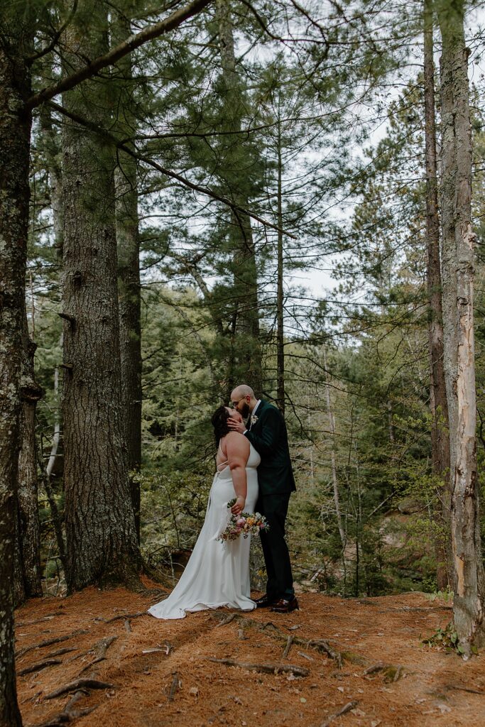 husband and wife share a passionate kiss under tall trees by Minnesota elopement photographer