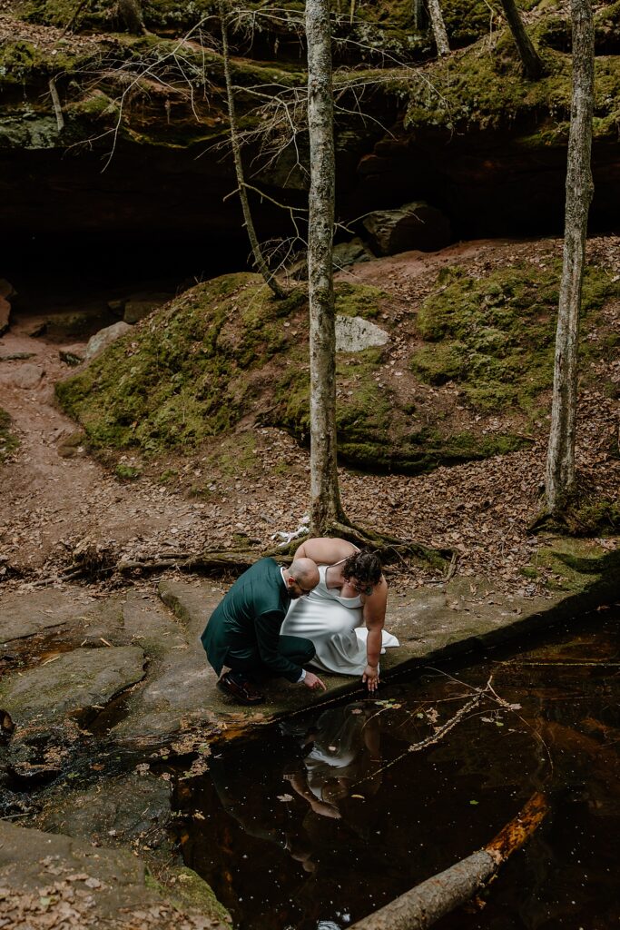 couple leans down to look at creek by Minnesota elopement photographer