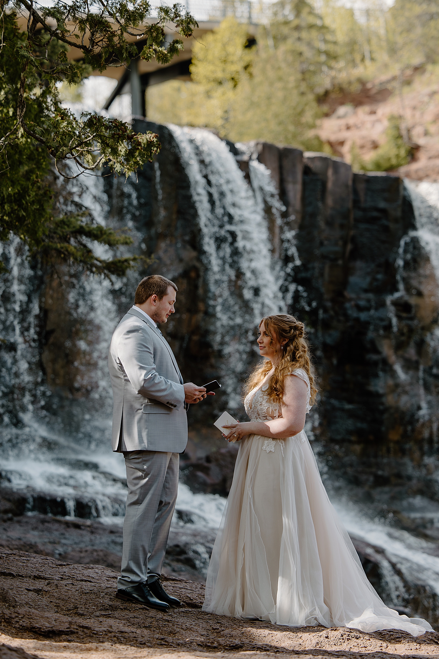 man and woman stand in front of water during the best time to elope at gooseberry falls state park