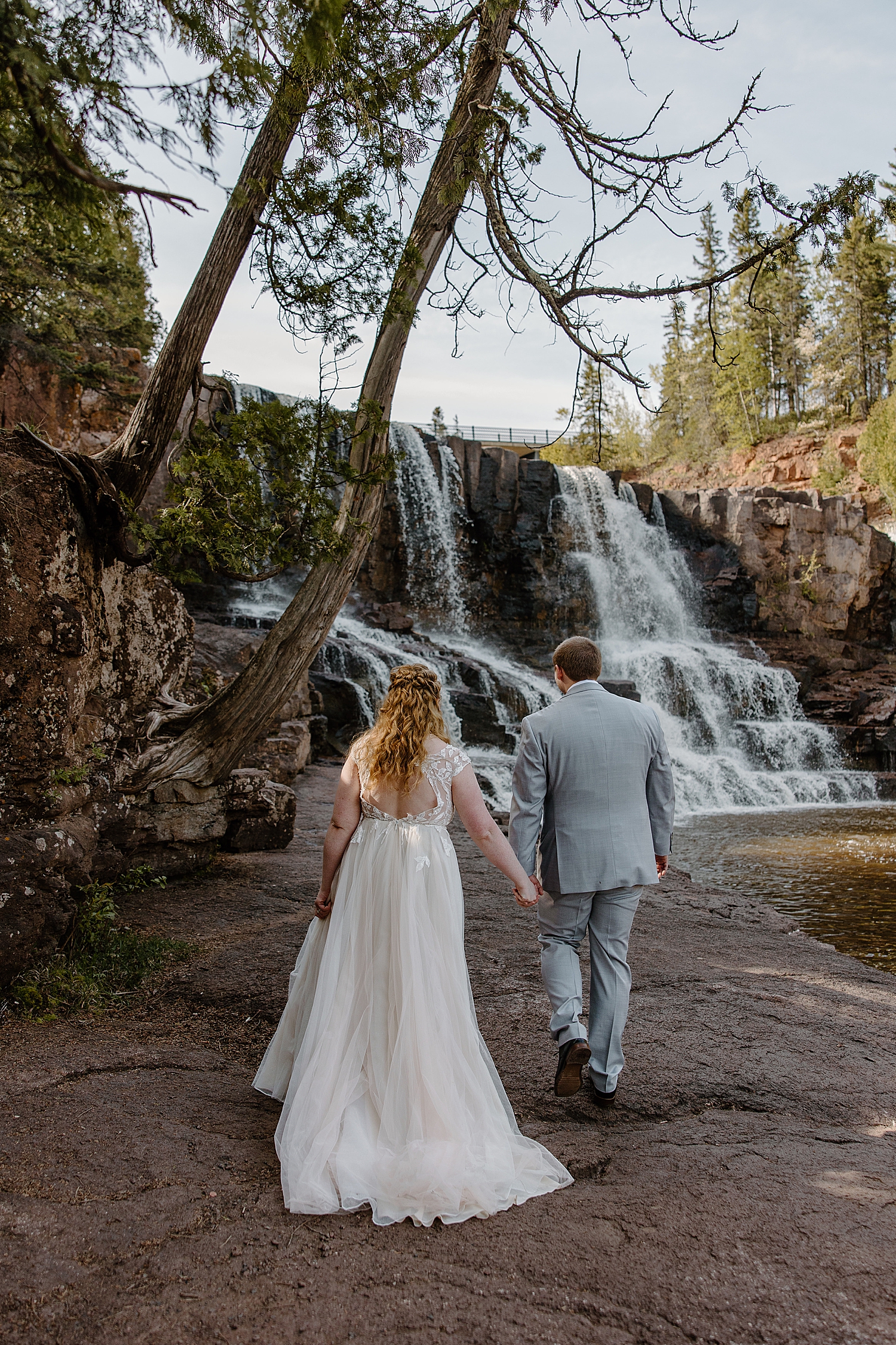 newlyweds walk toward water during the best time to elope at gooseberry falls state park