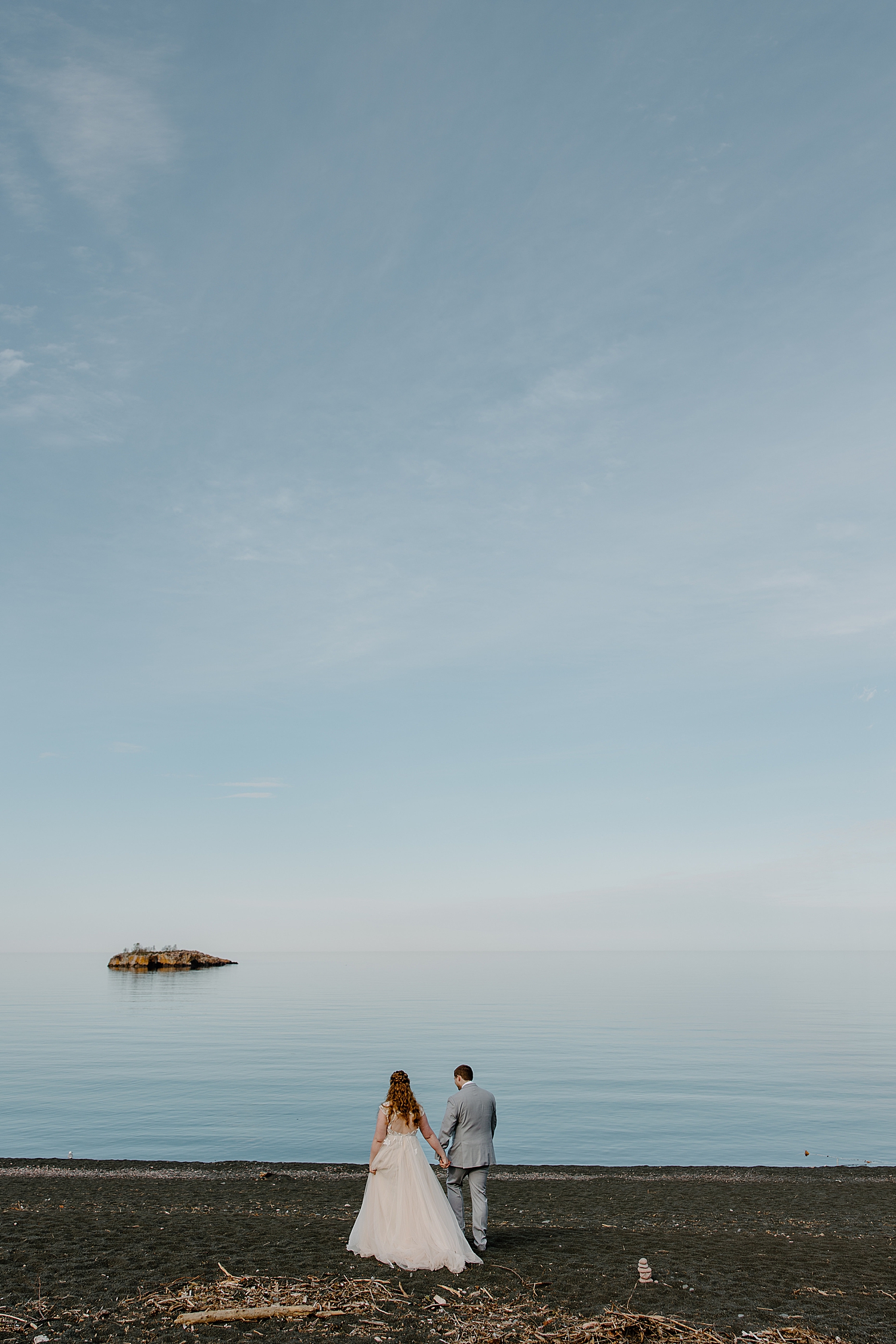 husband and wife walk hand in hand by water by Minnesota Elopement Photographer