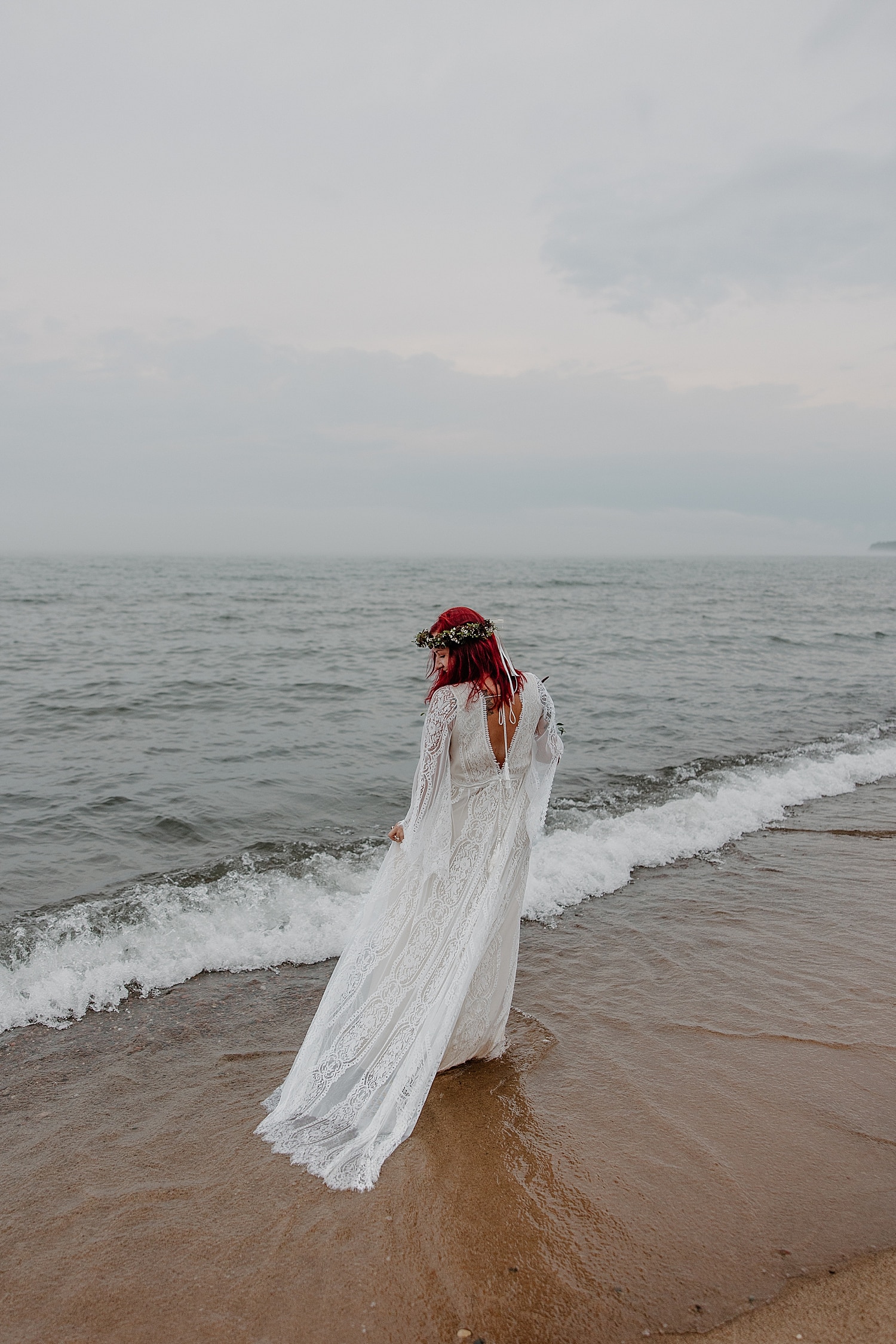 redhead bride in flowy boho gown stands on shoreline for Wisconsin Beach Elopement