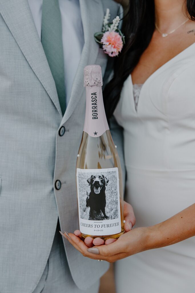 bride and groom hold custom wine bottle showing how to include pets in your elopement