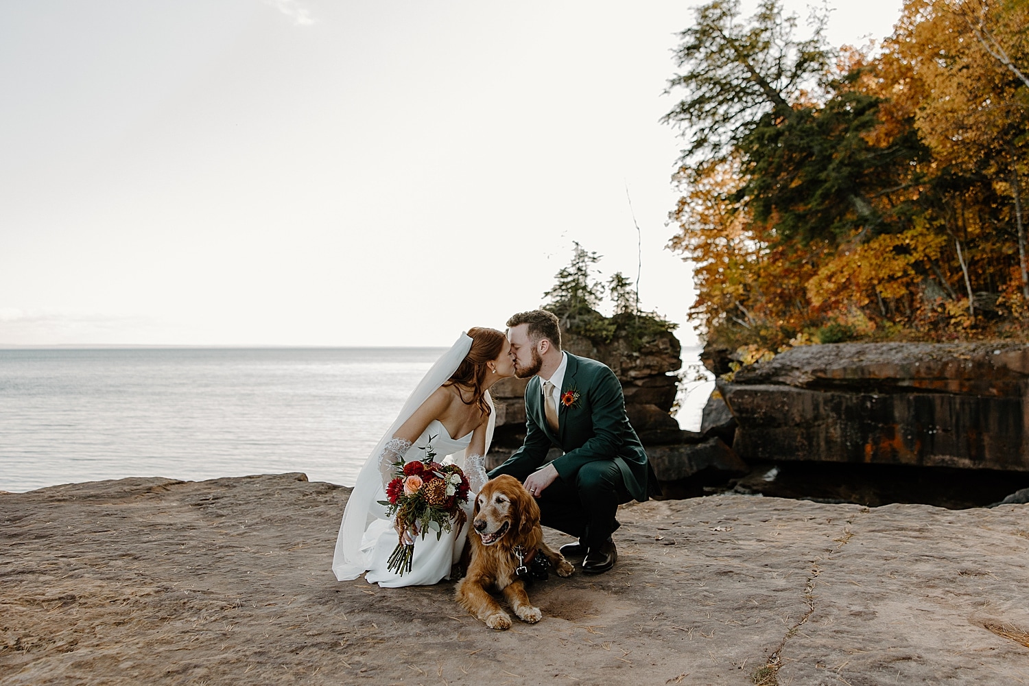 couple kiss on cliffside next to pup showing how to include pets in your elopement