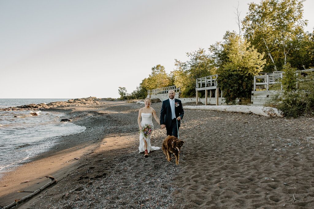 husband and wife in formal attire walk on beach with pup by Samantha Burke Photography