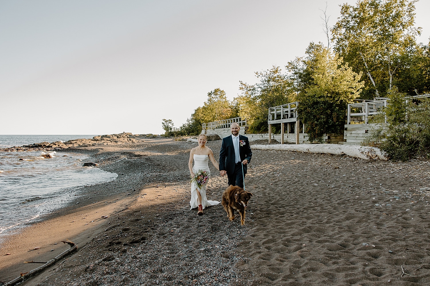 husband and wife in formal attire walk on beach with pup by Samantha Burke Photography