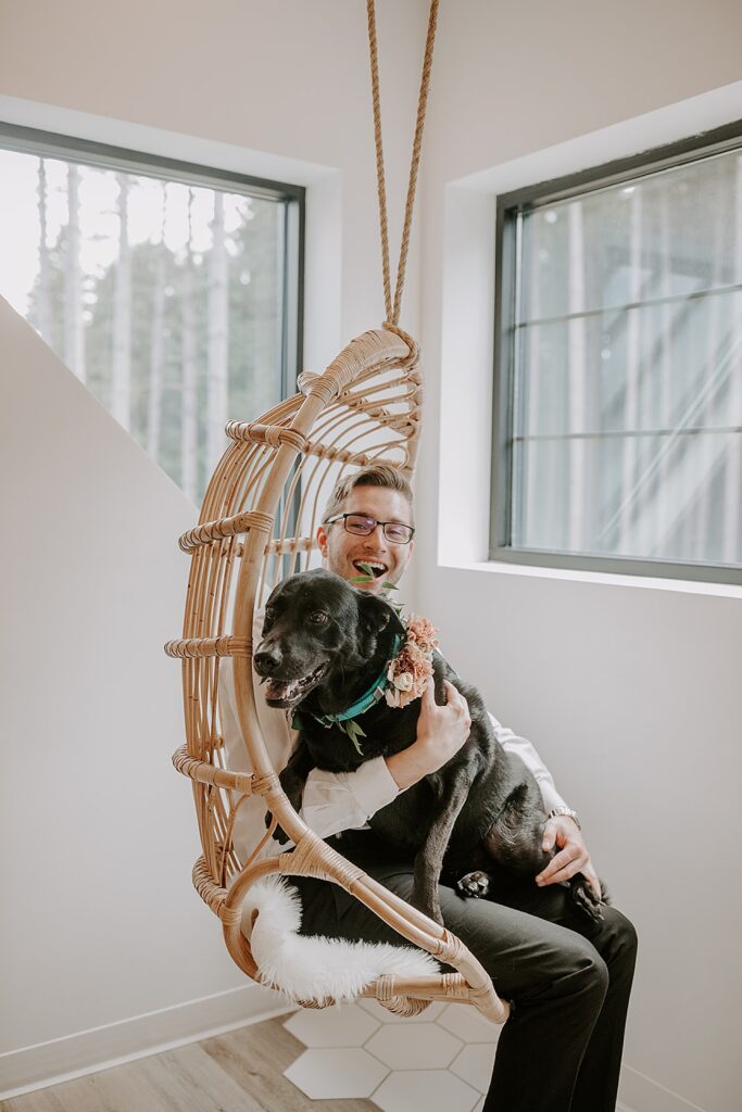 groom sits in swing chair with large black lab on his lap by Wisconsin wedding photographer