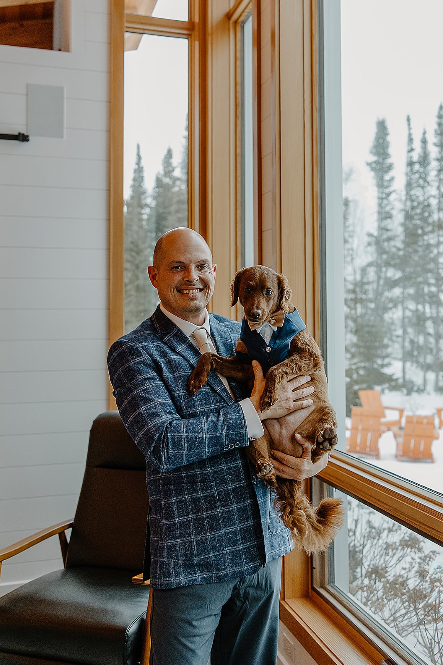 man in blue suit holds up pup next to windows by Wisconsin wedding photographer