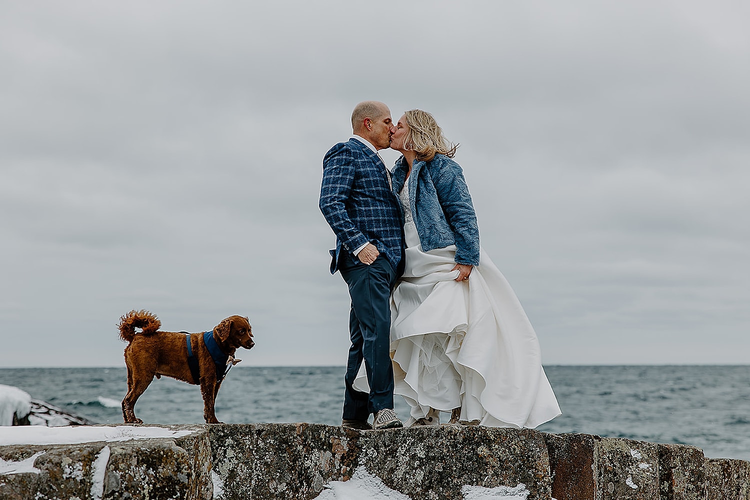 couple kiss on snowy cliffside next to water by Wisconsin wedding photographer