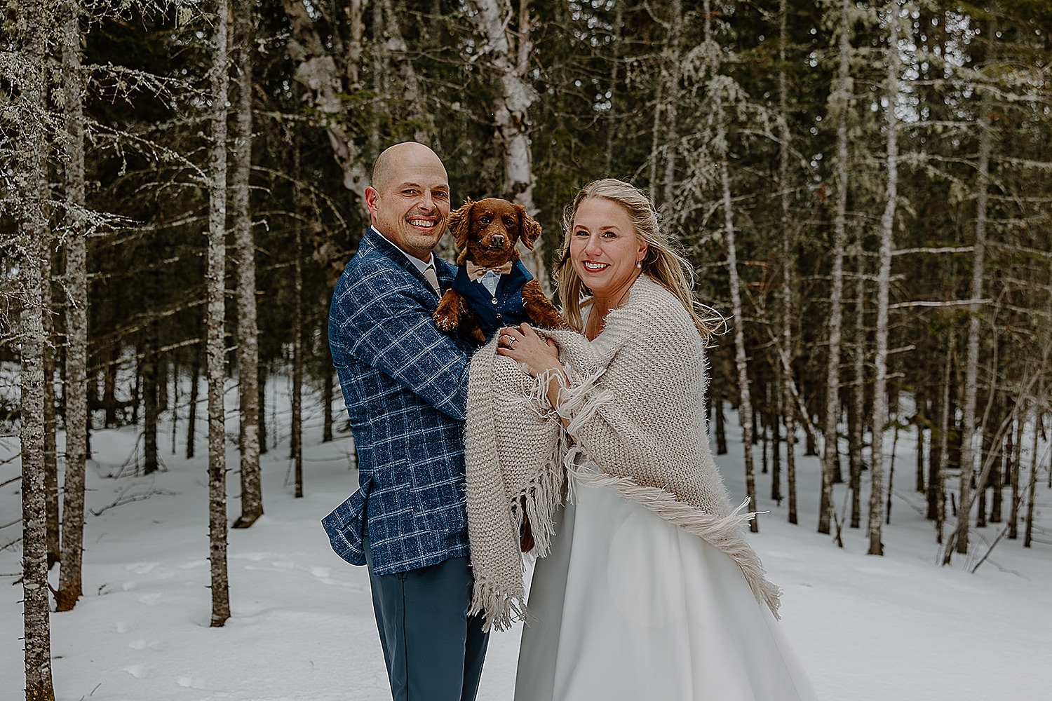 winter bride and groom stand in the trees holding their pet by Wisconsin wedding photographer