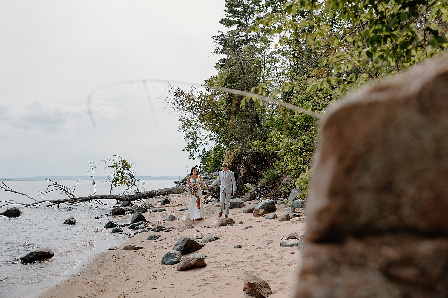 bride and groom walk the shoreline for Lake Superior intimate wedding