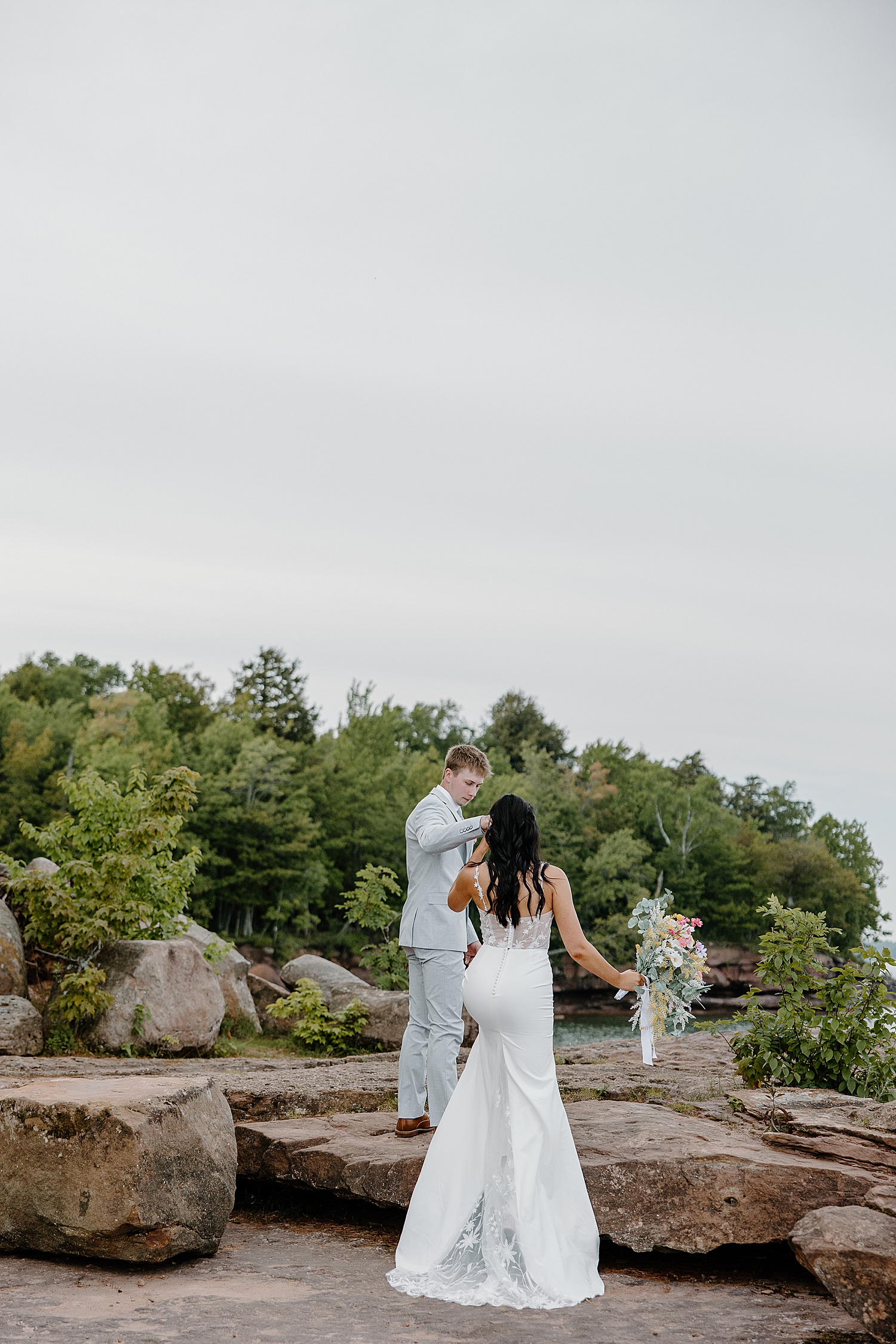 man helps woman up rock for Lake Superior intimate wedding