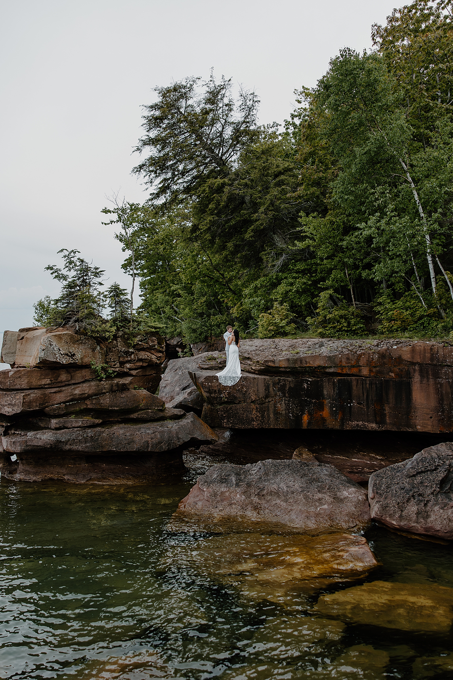 Bride and groom stand on cliff edge over water by Minnesota elopement photographer